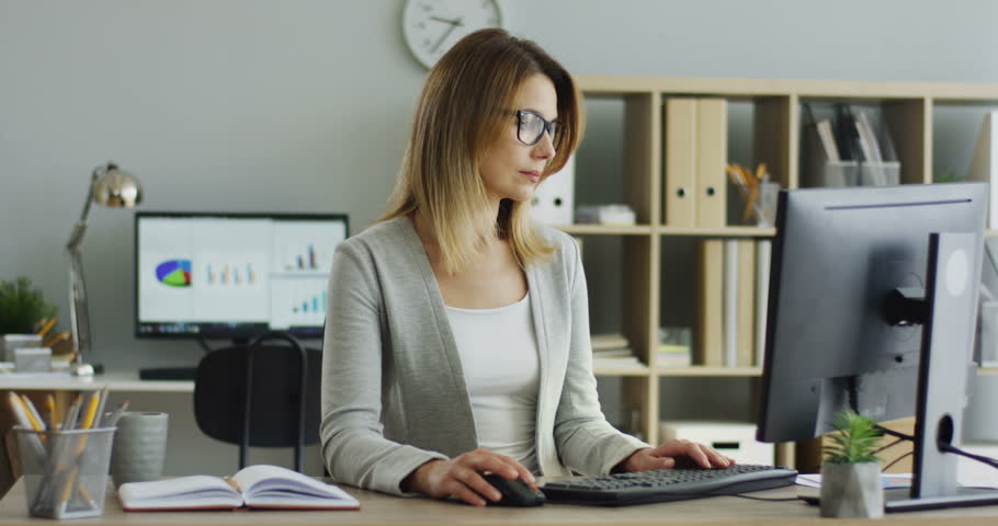Portrait shot of the succesful businesswoman boss being in her office at the desk with computer and typing on its keyboard.