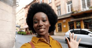 POV of beautiful African American joyful woman in good mood video chatting while standing on street. Close up portrait of happy female speaking on video conference outdoor in city. Conversation