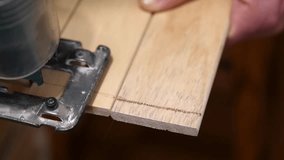 Close-up video footage of a man sawing wooden boards with an electric jigsaw. Working with wood during renovation or construction. The worker repairs or makes furniture.