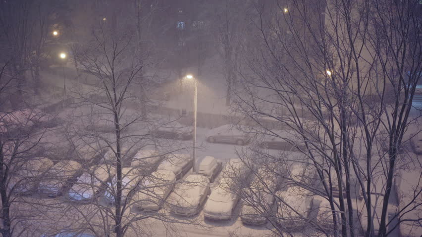 Evening snowfall in the city. Aerial view of the parking lot. Streetlights.