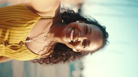 VERTICAL VIDEO, Close-up portrait of smiling girl with long curly hair chatting on the embankment, on yacht background. Frontal closeup of happy young woman using mobile phone