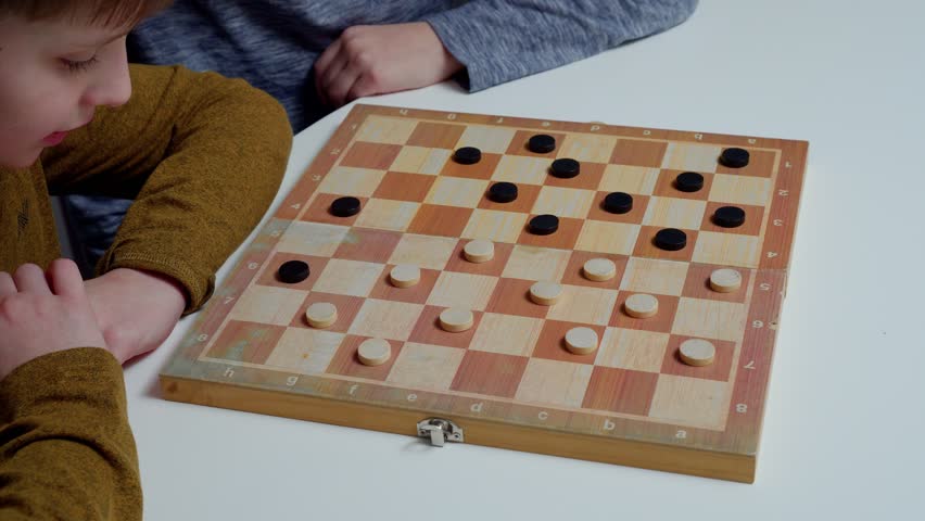 Unrecognizable preteen schoolboys children sitting at white table, playing checkers on wooden board, planning, building strategy, teaching, learning. Board games, gaming, education, entertainment.