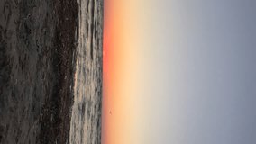 Vertical video of time lapse of sunrise over calm sea with waves, sandy beach and flying seagulls. Dawn over horizon, ocean, water - timelapse or hyperlapse. Red clear sky
