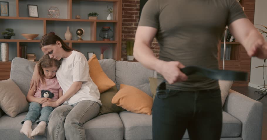 Man abuser holding belt while mother hugging daughter on sofa
