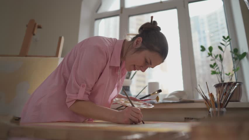 Art, creativity, hobby and creative occupation concept. Bringing creativity to life. Woman painting in art studio. Attractive female artist painting in workshop. Woman hobby, activity, profession. | Shutterstock HD Video #1099279949