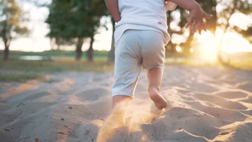Feet running on the sand on beach. Child runs in the sun. Happy summer vacation. Child picnic in park. Bare feet of a toddler on the beach. Family vacation in nature. Cheerful kid playing in the park Royalty-Free Stock Footage #1099280317