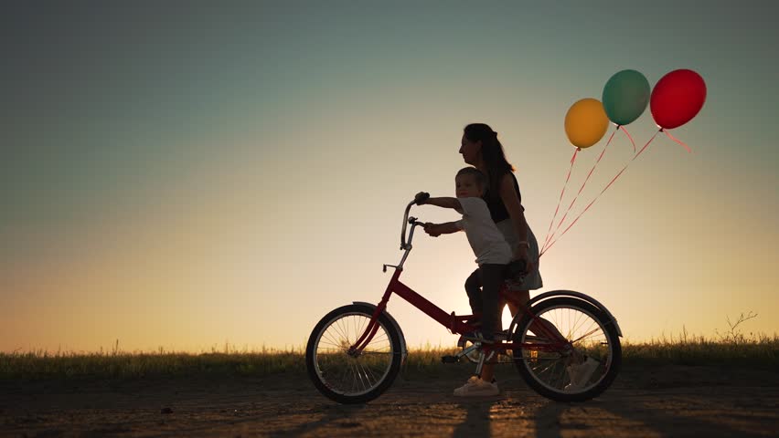 Happy family. Mom teaches son to ride bike. Concept of children holiday and dreams. Family playing in park at sunset. Silhouette of mom and son on a bike in the park. Green energy. Mom teaches son. Royalty-Free Stock Footage #1099280351