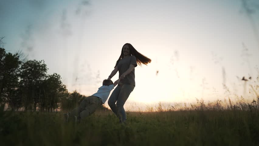 Happy family concept. Mom and son are playing in the park at sunset. Mom with a child together holding hands circles baby. Family vacation at sunset. Family playing outdoors active in summer evening.