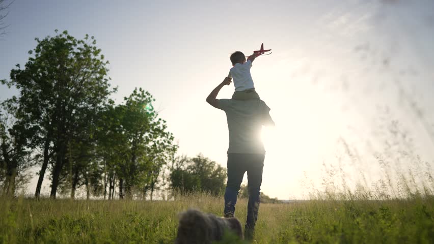 Father's Day. Family walk in the park with a dog. Boy sits on his father shoulders with toy airplane. Walk with your pet at sunset. Child with wind toy airplane around his father neck. Summer walk | Shutterstock HD Video #1099280449