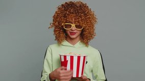 Excited young teenager school girl in 3D glasses eating popcorn, watching interesting tv serial, sport game, film, online social media movie content. Curly haired child kid on studio gray background