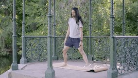 Young latin hippie man with long hair and sportswear standing on a mat stretching the lateral side of the body. 4k video.