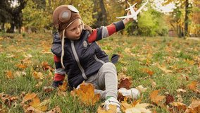 Child pilot aviator with airplane dreams of traveling in nature. Boy playing with a toy plane at park on a sunny day. Little cute boy play with airplane in park outdoors. Boy holding toy plane