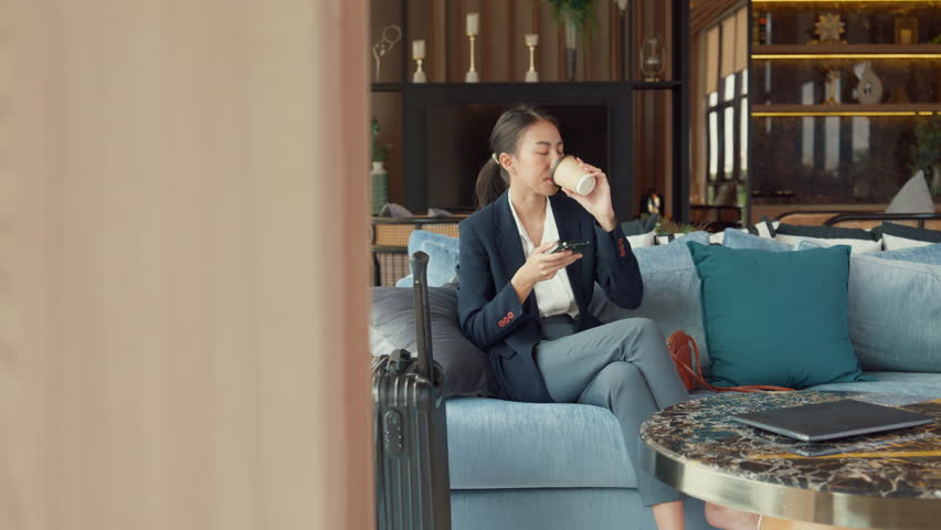 Youth Asia business female passenger wear suit sit on couch chair drink tea play phone look online booking ticket in modern airline lounge wait for transit at airport. Travel business trip concept. Royalty-Free Stock Footage #1099294675