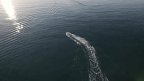 Aerial drone pursuit of a small sailing boat splashing water in the Mediterranean Sea towards the sun