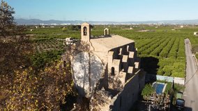 4K drone footage of a flight over an ancient church among orange trees in Spain