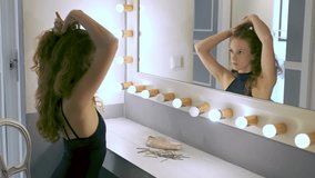 Young ballerina fixing her hair into a pony tail in front of the mirror.