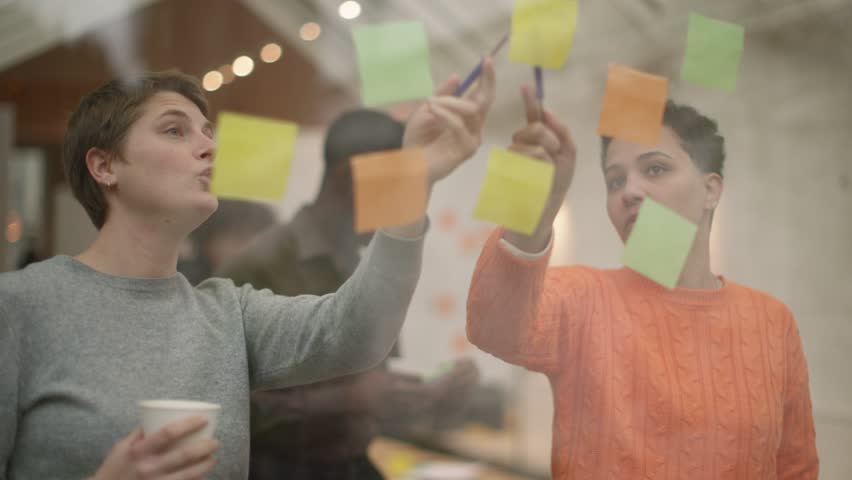 Young Minds in Action: Idea Exchange - group of multicultural young colleagues exchange ideas using adhesive notes on window Royalty-Free Stock Footage #1099300903
