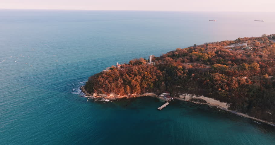 Aerial view Beautiful panorama nature of picturesque cape in sea with bright vegetation trees forest with cottages background of blue sky and sea water lighthouse at sunset in autumn on clear day