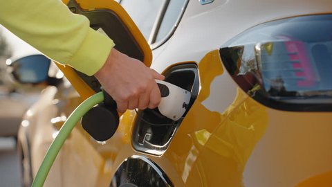 EV Car or Yellow Electric car charging station man's hand pulls out power cable closes lid in warm light of lens flares at sunset. Car sharing commuter charging station  Alternative energy Stock Video