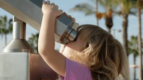 child in pink T-shirt looks through stationary city binoculars in park. Funny curly blonde girl holds her hands on large binoculars after paying with coins. Beautiful view through spyglass in city. - Powered by Shutterstock - Get 15% off with code: PIKWIZARD15