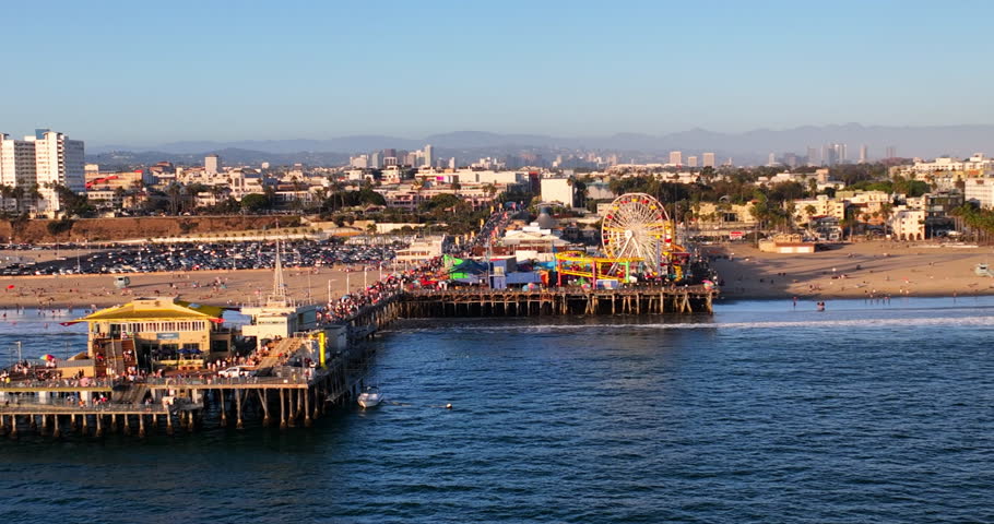 Aerial Shot Of Famous Fishing Pier And Amusement Park At Beach, Drone Flying Backwards Over Sea In City - Santa Monica, California