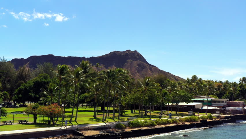 Aerial Forward Shot Of People Walking By Palm Trees Against Mountain During Sunny Day - Oahu, Hawaii