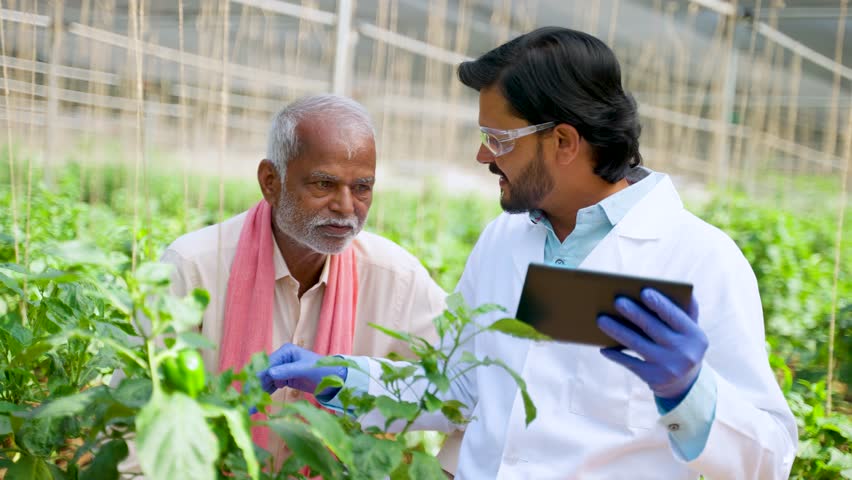 Agro scientist explaining crop growth from digital tablet to farmers while sitting at greenhouse - concept of modern farming, technology support and cooperation.
