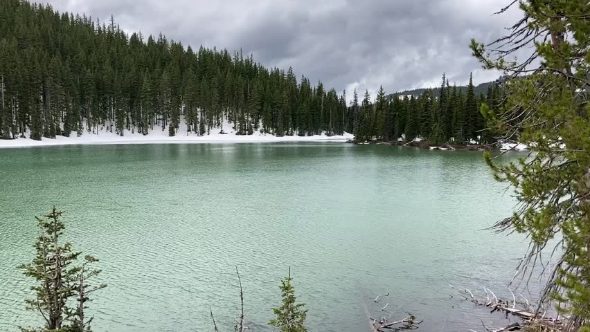 The beautiful aqua Devils Lake, surrounded by evergreen trees and snowy hills, on the Cascade Lakes Scenic Byway. Taken on a cold, overcast day - Nr Bend, Oregon, USA