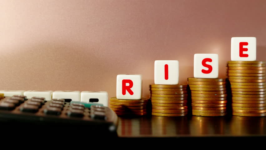 Generic rate rise concept (eg, bank or interest or inflation) - A calculator lining up the word ‘rate’ made with letter dice, next to the word ‘rise’ on columns of coins. Royalty-Free Stock Footage #1099315935