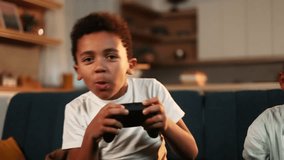 Excited cute little boy kid with joystick controller playing video games in the late evening at home alone Happy child have fun relax after school lessons indoors Game addiction concept
