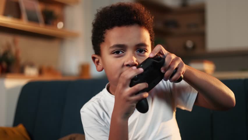 Excited cute little boy kid with joystick controller playing video games in the late evening at home alone Happy child have fun relax after school lessons indoors Game addiction concept | Shutterstock HD Video #1099319089