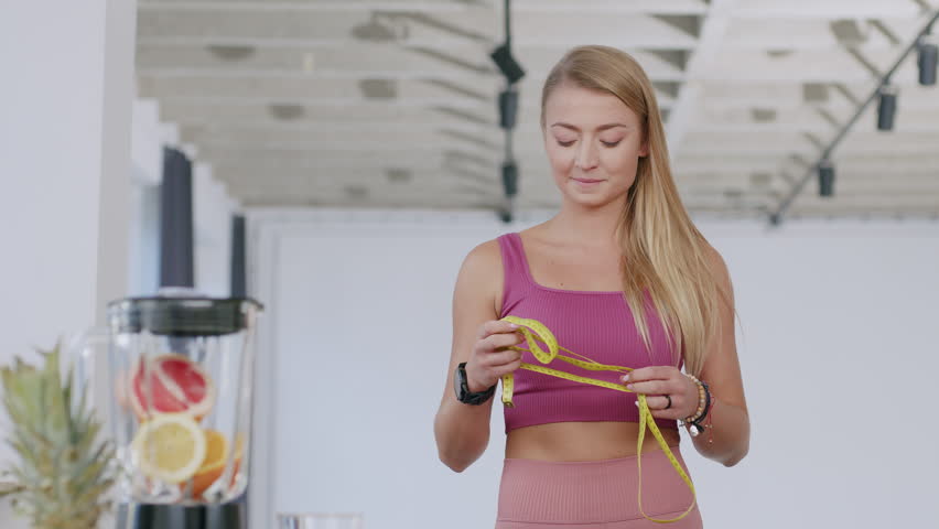 A young beautiful caucasian woman smiles at the camera holding the tape measure - a healthy living concept | Shutterstock HD Video #1099319565