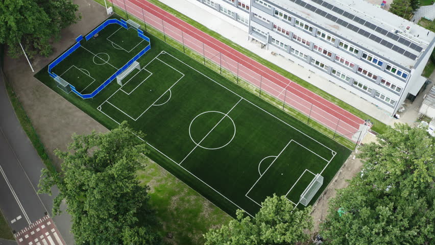 Flying backwards aerial shot of a brand new soccer field and running track next to the elementary school in Poland, 4K drone