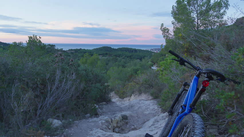 Mountain bike parked on dirt track leading downhill toward stunning early morning sky and sea views at horizon.