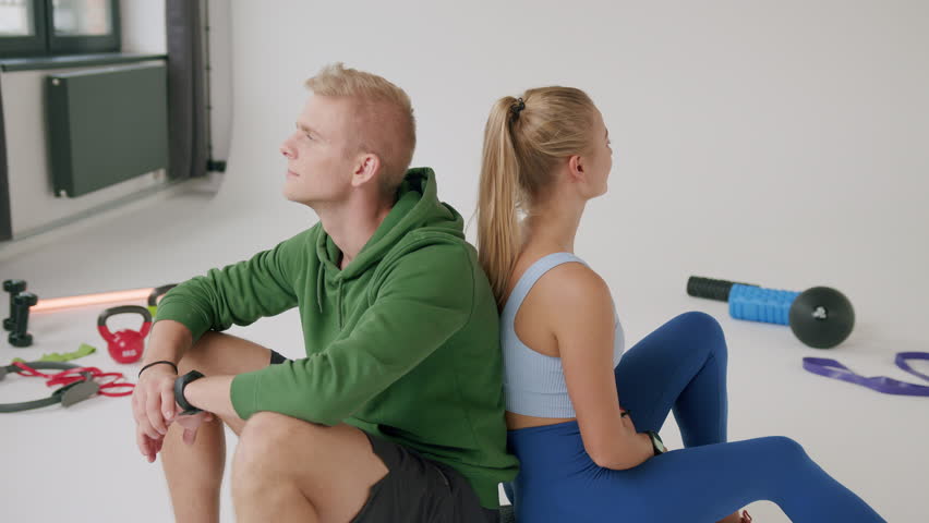 A young beautiful caucasian woman sits with a personal trainer in the private gym and looks and smiles at the camera | Shutterstock HD Video #1099319803