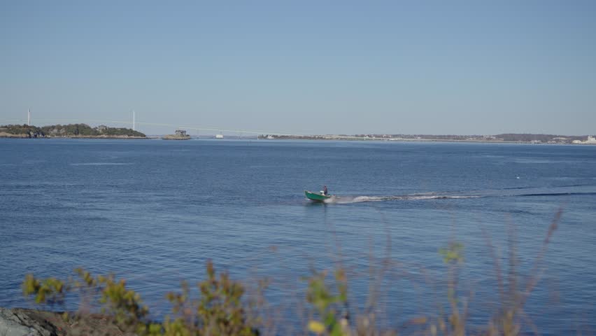 Man driving a small boat in the ocean offshore in Newport Rhode Island. Small green motorboat drives by in a saltwater cove.