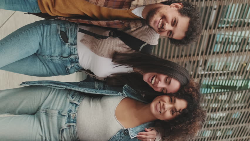 VERTICAL VIDEO, Young smiling people posing while standing on the street. Four students look at the camera and smile. Royalty-Free Stock Footage #1099320617