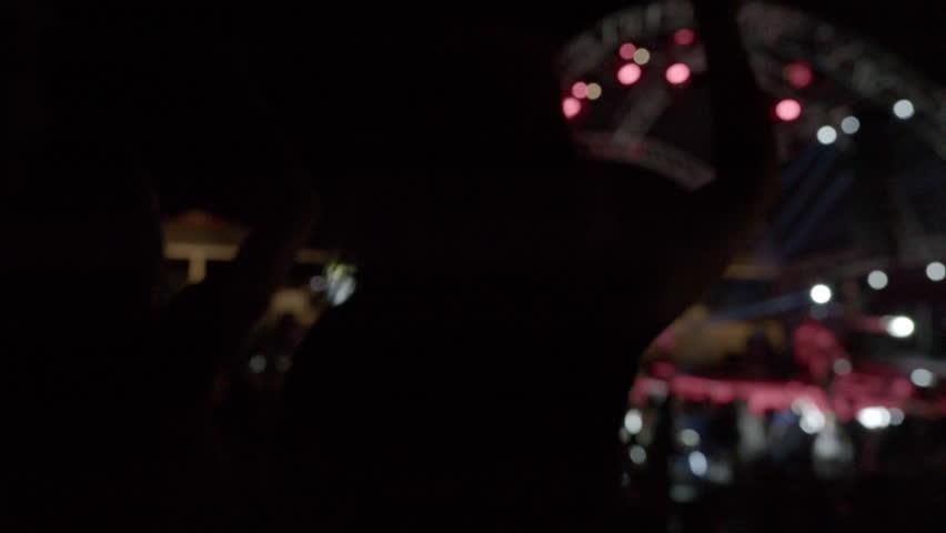 A night concert of a musical group. In the foreground, a group of teenagers are dancing. Silhouettes. Bright platform at a night party.