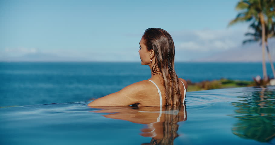 Woman relaxing in luxury infinity pool looking out at the ocean, tropical resort spa vacation Royalty-Free Stock Footage #1099328767