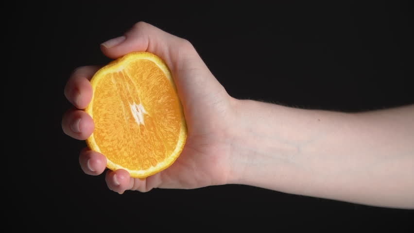 Close-up of female hand squeezing an orange. Person pressing a juicy fruit without a juicer. High quality 4k footage Royalty-Free Stock Footage #1099331599