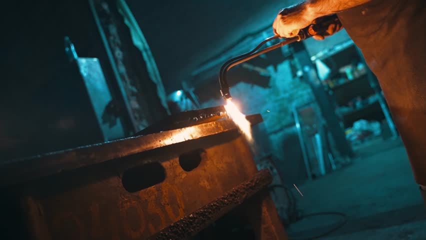 An employee cuts a piece of metal with a torch. | Shutterstock HD Video #1099332475