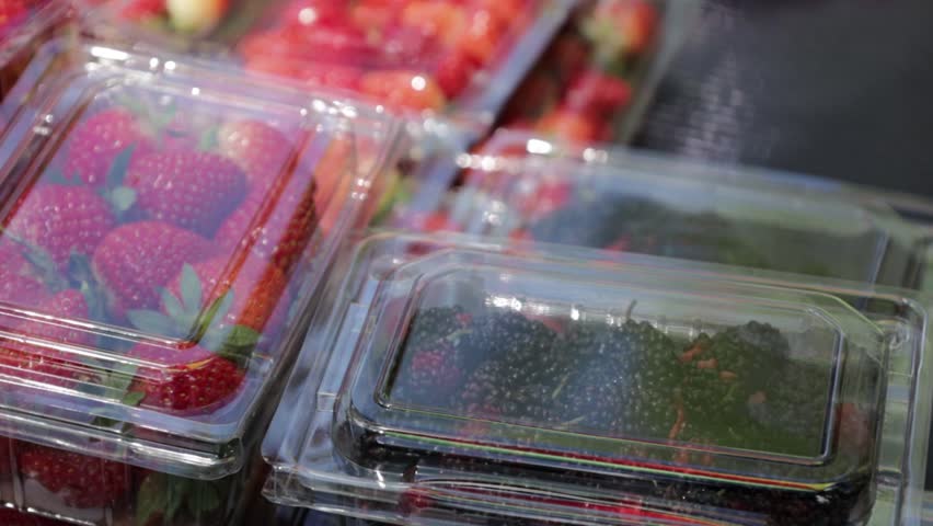 Fresh blackberries and strawberries in the closed plastic containers ready for sale. Fresh healthy fruit