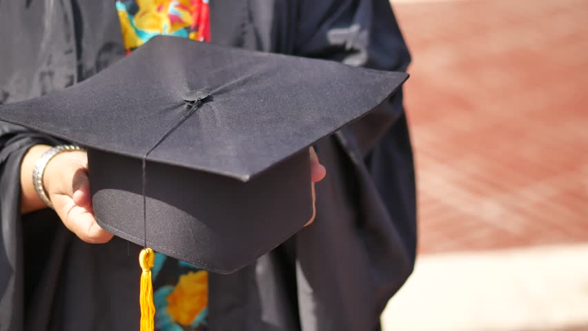 Student hold hats in hand during commencement success on yellow background 