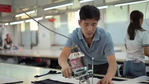 Ba Ria, VIETNAM - JAN 19 2023: Man with cutter machine and personal protective equipment at garment industrial work place. Fabric cutter in Asian textile garment factory Video de contenido editorial de stock