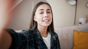 Smiling young caucasian woman vlogger make video call, looking at camera, recording vlog at home, talking. View from front camera to portrait video recording, girl holds mobile phone in hands.