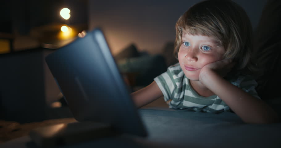 Curious cute kid boy using digital tablet technology device lying in living room.dolly shot Small child hold pad computer surfing internet play game at home. Children tech addiction concept | Shutterstock HD Video #1099342735