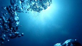 Underwater air bubbles rising from deep water up to the surface in tropical sea