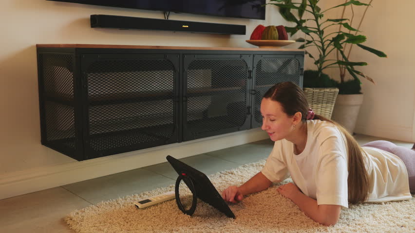 Young woman switches on air conditioner with heating mode after using tablet lying on furry carpet. Fast and safe way to warm up room. Energy efficient and money saving heating solution. HQ 4k footage | Shutterstock HD Video #1099353225