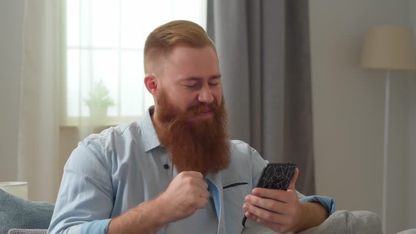 Happy Young Redhead Man Looking at Smartphone Screen | Shutterstock HD Video #1099353517