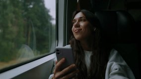 A young woman wearing headphones watches a video on her phone while traveling by train